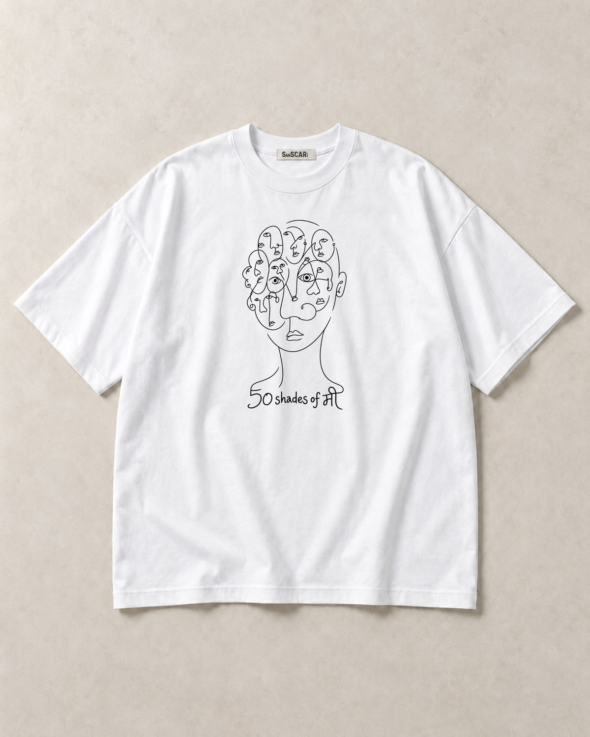 50 Shades of मी white oversized tee laid flat on a stone background