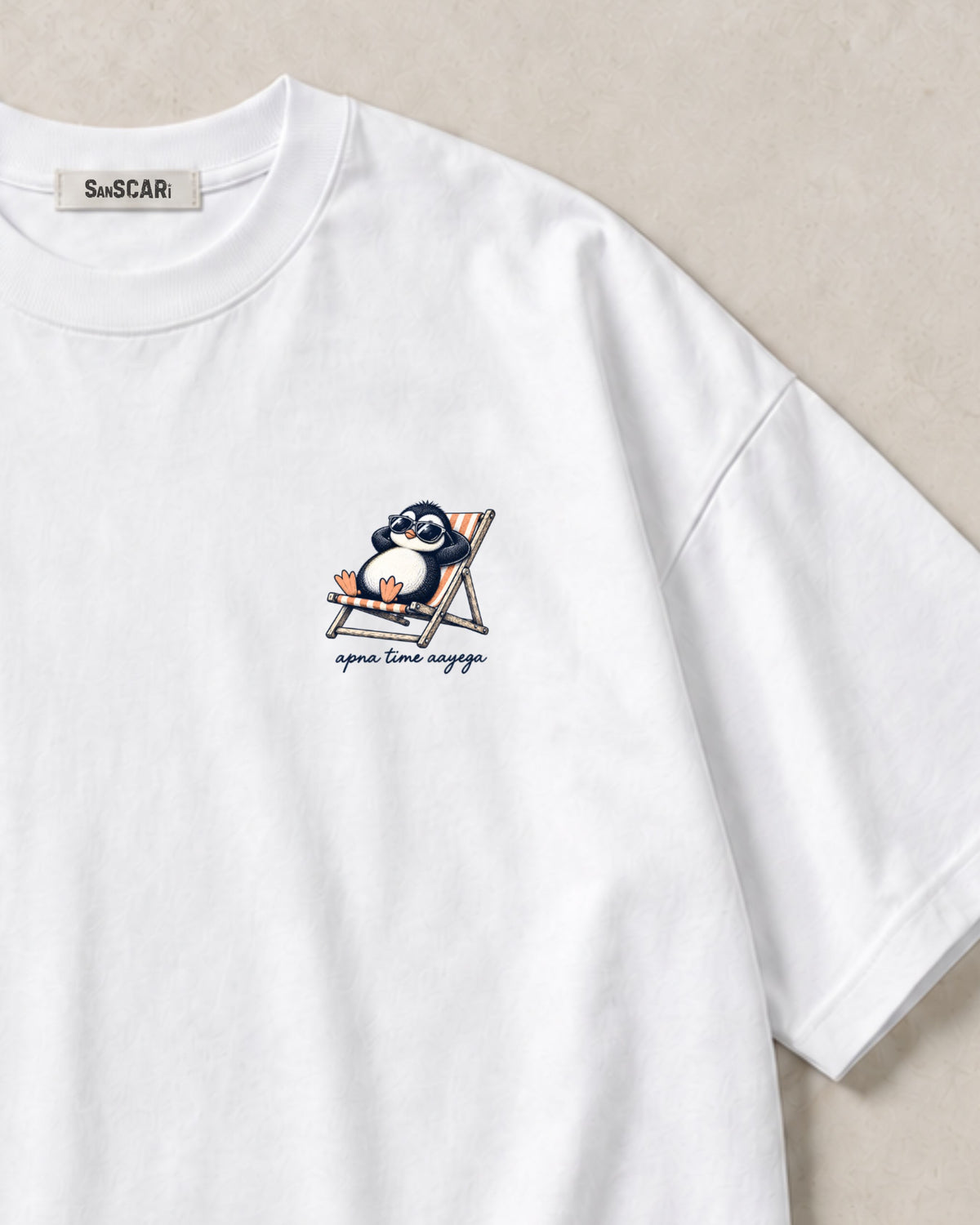 Apna Time Aayega white oversized tee laid flat, close-up of the penguin print